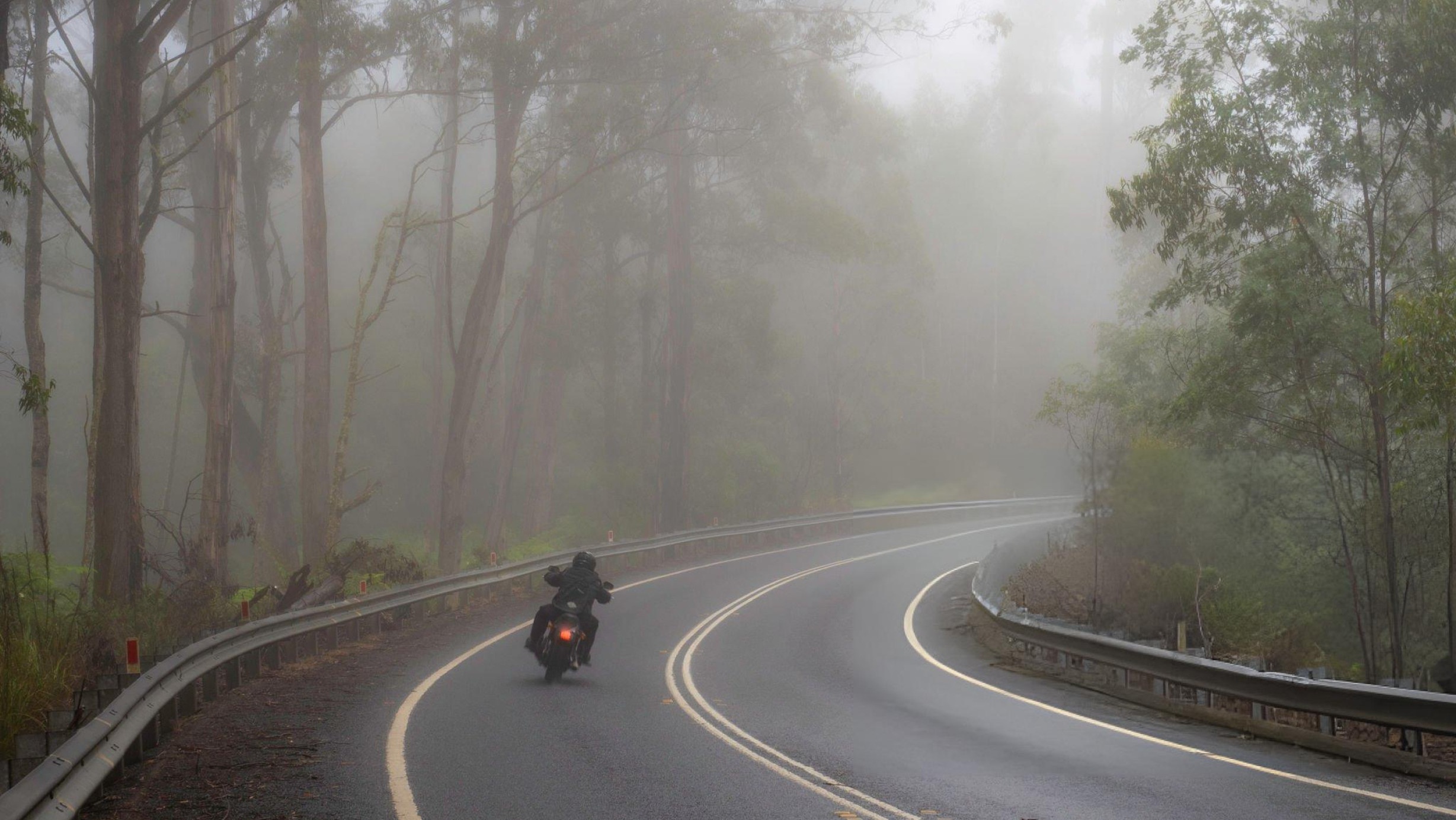 Hero image of a motorcyclist riding in steady rain with waterproof gear and high‑visibility accents, emphasizing safety and control